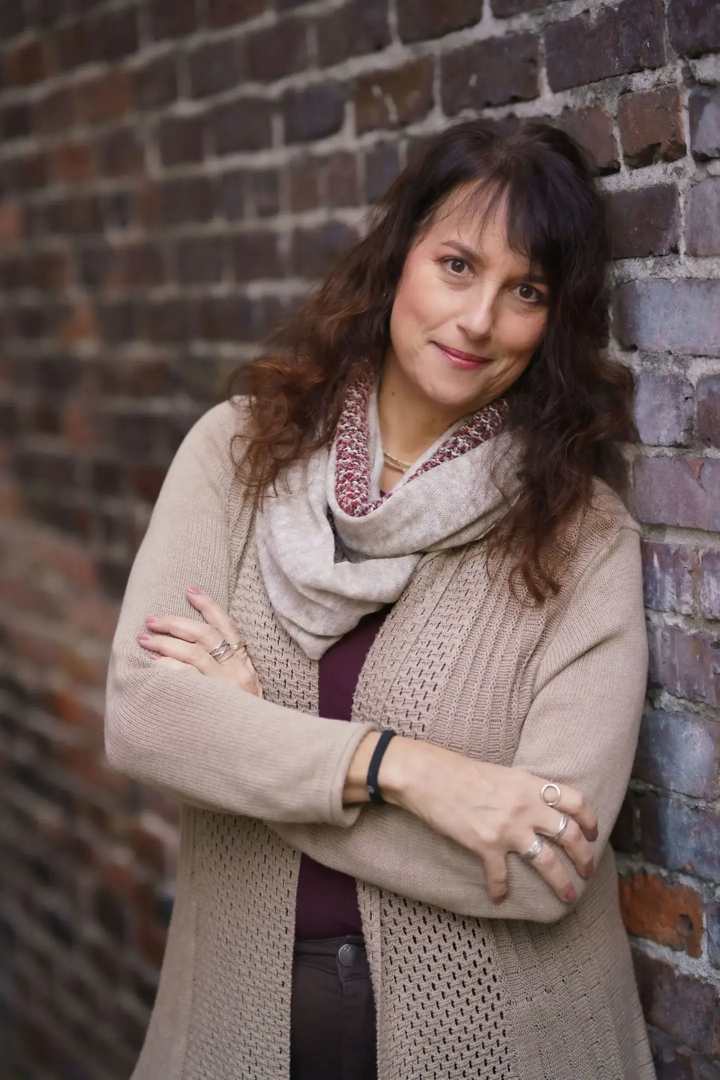 Issy Kleiman, MA, LMFT, AAMFT Approved Supervisor, standing with her arms crossed against a brick wall in a camel cardigan